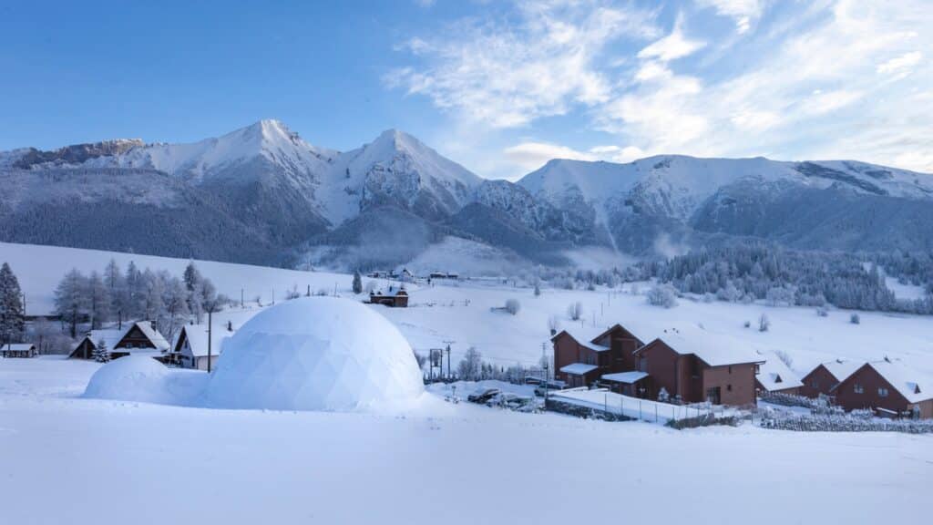 Iglu zu sehen, verschneite Landschaft, im Hintergrund ein Dorf