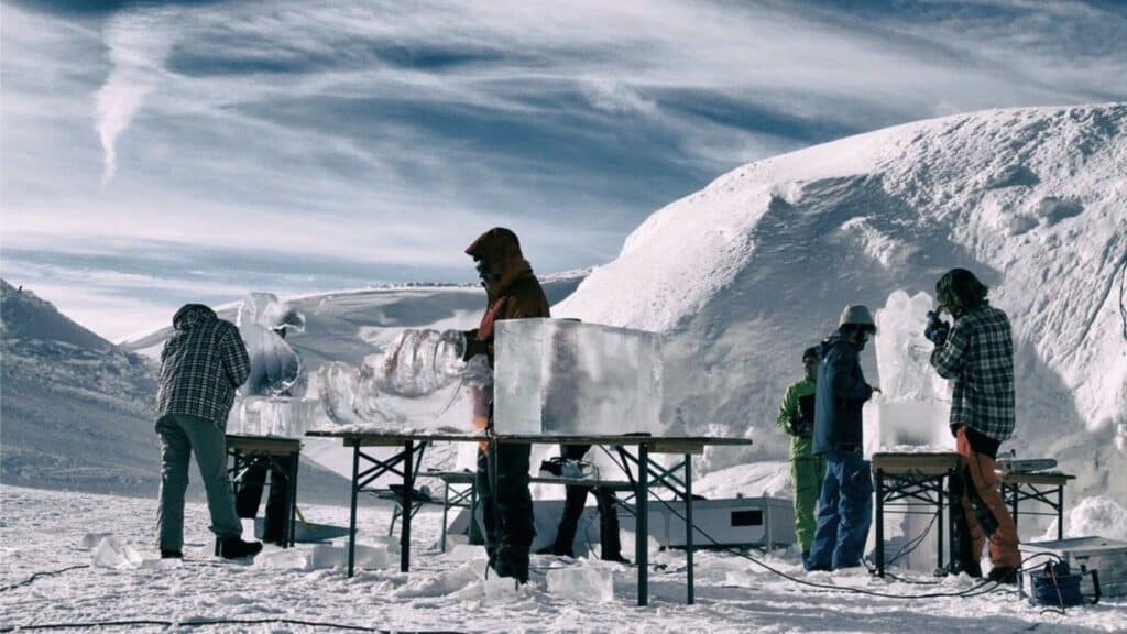 Menschen stehen im Schnee mit Bierbänken und schnitzen Eis