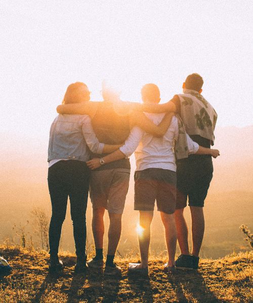 Gruppe von Menschen steht umarmt im Sonnenuntergang – Symbol für Zusammenhalt und Gemeinschaft beim Teambuilding in Bayrischzell