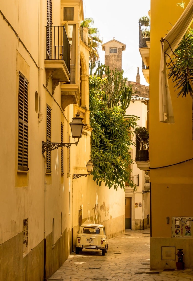 Schmale, sonnendurchflutete Gasse in Palmas Altstadt mit historischen Fassaden und einem geparkten Oldtimer – authentisches Stadtmotiv für eine Incentivereise Mallorca.